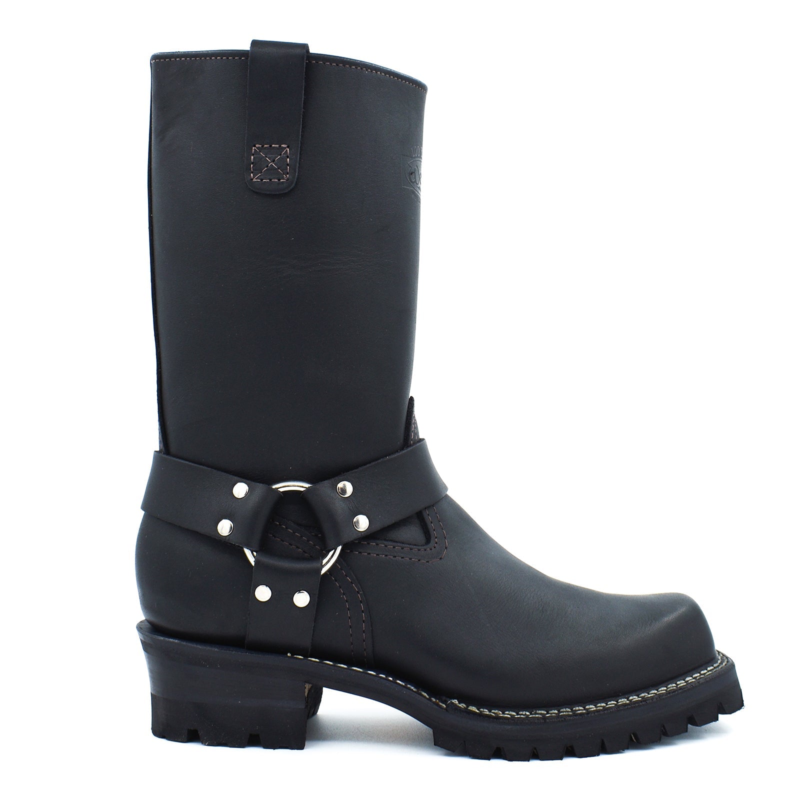 Side profile of black harness engineer boots displaying wide mouth tall shaft, rear pull strap with contrast brown topstitching, and cross-stitch leather badge patch