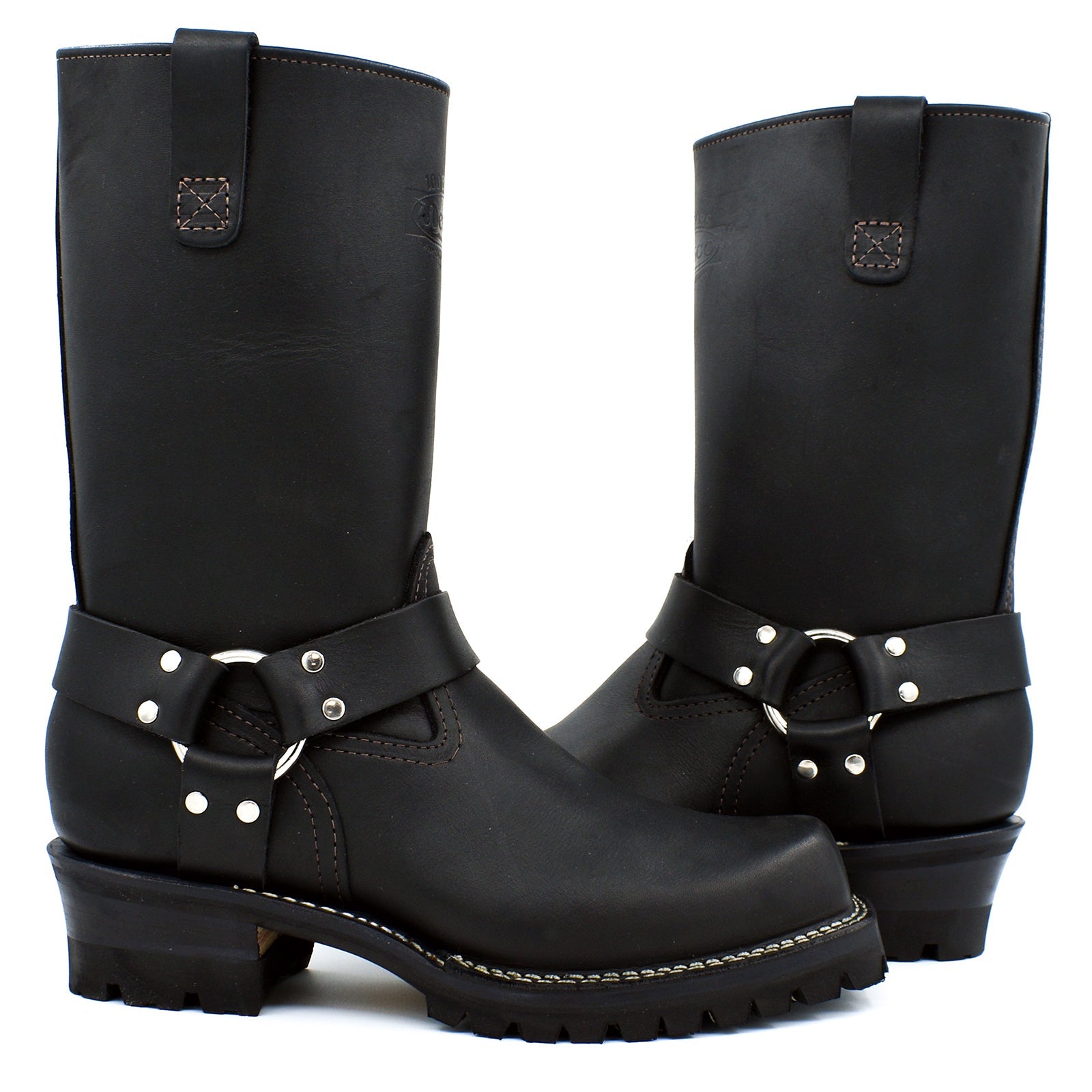 Black oiled leather tall shaft harness engineer boots with chrome D-ring and polished nickel stud double strap ankle harness system on white background