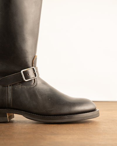 Close-up of gunmetal silver rectangular single buckle on black leather ankle strap of tall aviator engineer boot