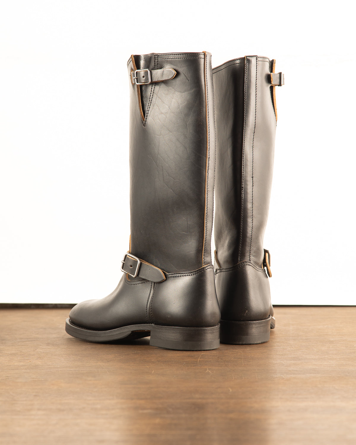Side profile of black aviator engineer boots displaying dramatically elongated tall shaft silhouette and single black leather ankle buckle strap