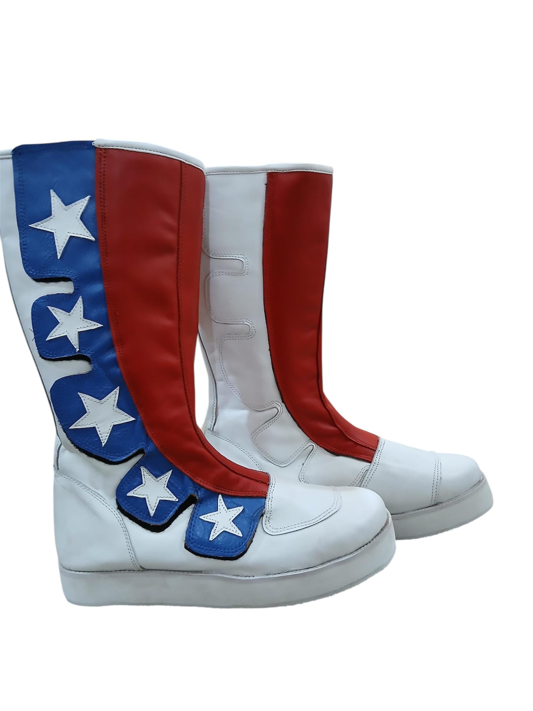 Red white and blue patriotic knee-high wrestling boots with cascading blue star appliqué panel and diagonal red stripe on white background