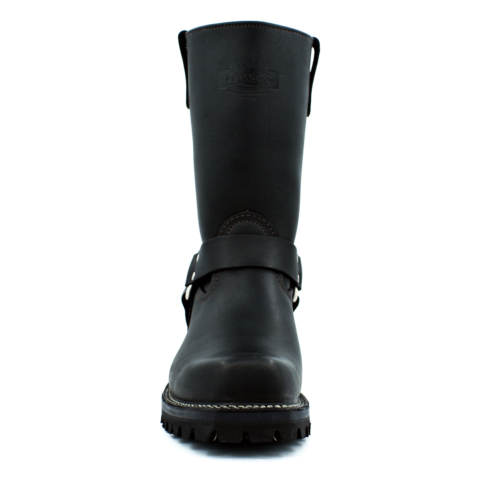 Front-facing pair of black biker engineer boots showing sculpted pointed-to-square toe box, full harness ring detail, and aggressive deep lug rubber outsole