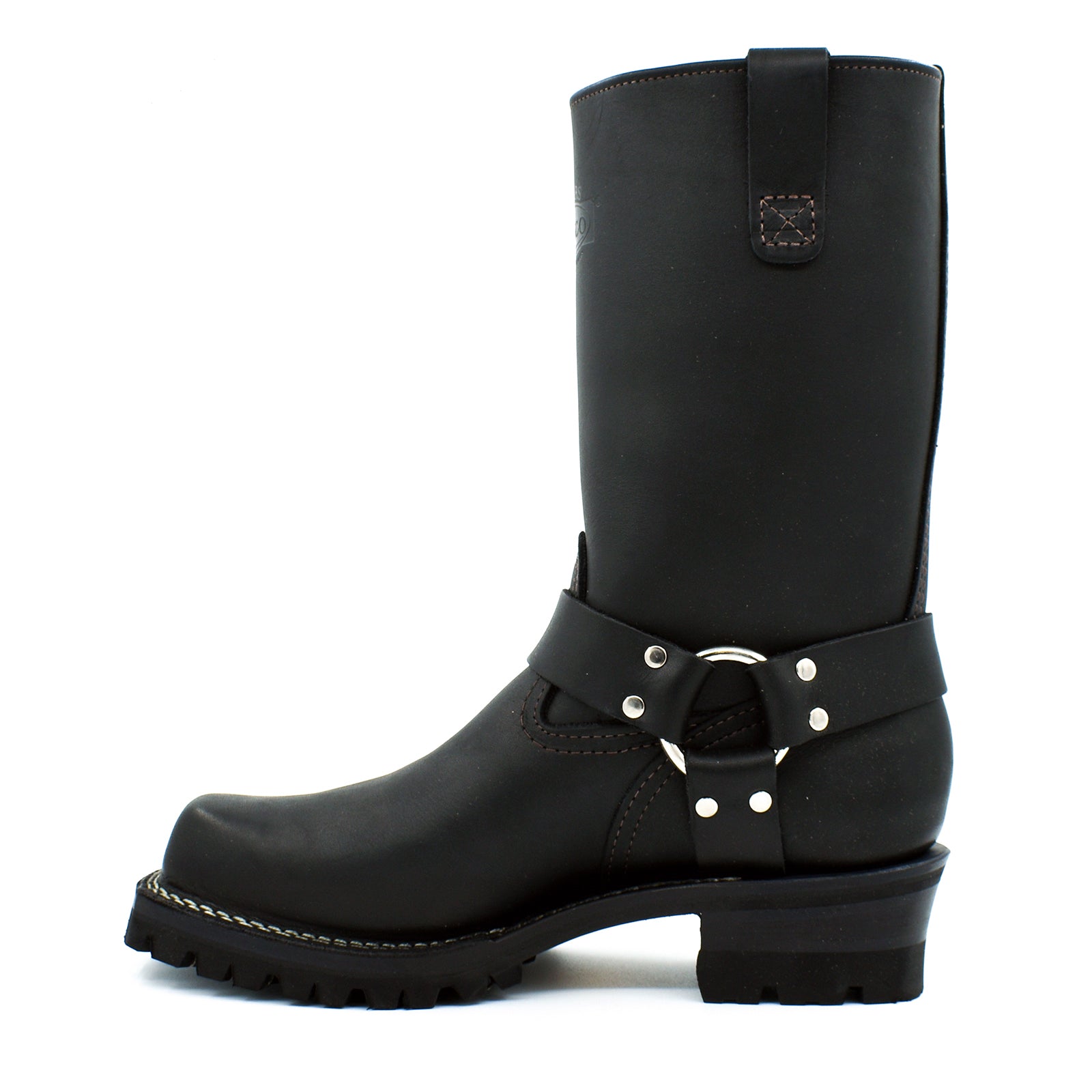 Close-up of chrome D-ring and polished nickel rivet harness strap system wrapping ankle of black oiled leather engineer boot