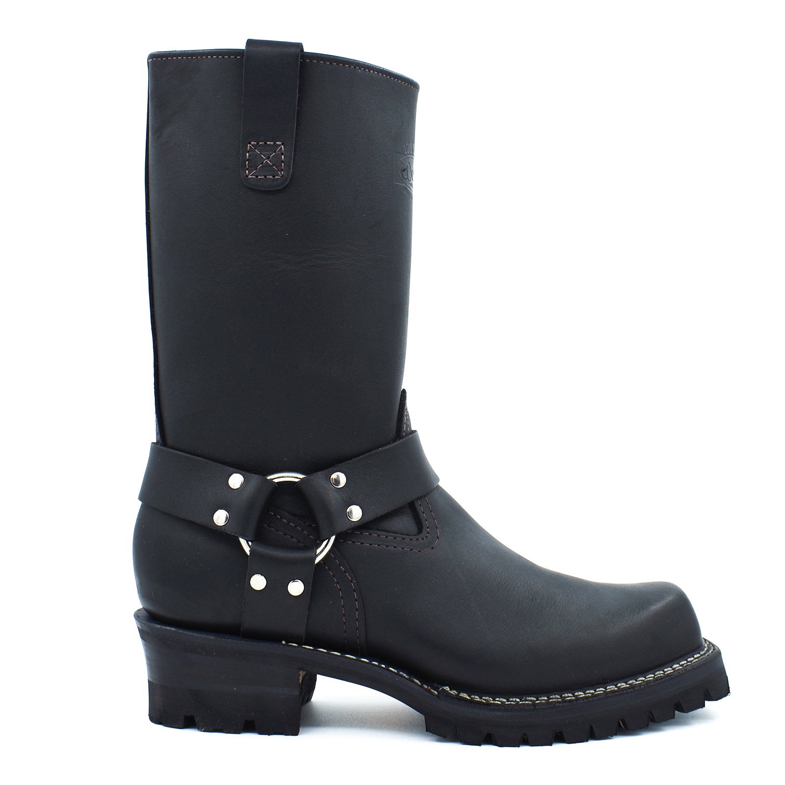 Side profile of black harness engineer boots displaying wide mouth tall shaft, rear pull strap with contrast brown topstitching, and cross-stitch leather badge patch