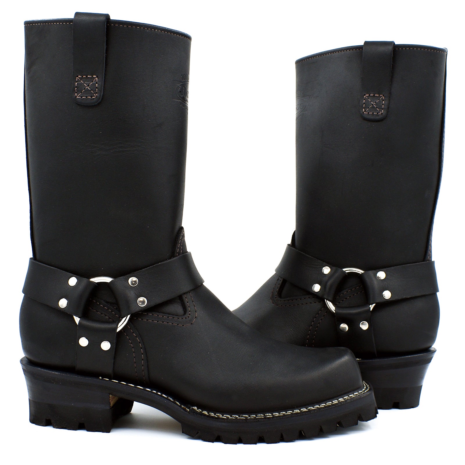 Black oiled leather tall shaft harness engineer boots with chrome D-ring and polished nickel stud double strap ankle harness system on white background