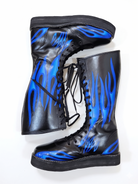 Front-facing pair of black inferno wrestling boots displaying vivid blue flame artwork covering both shaft panels and toe box